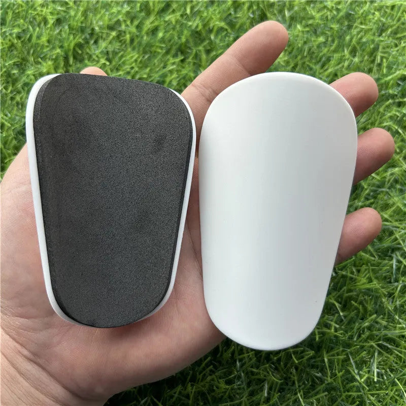 Extra small black and white plastic football shin guards for youth players, size 8cm by 5cm.