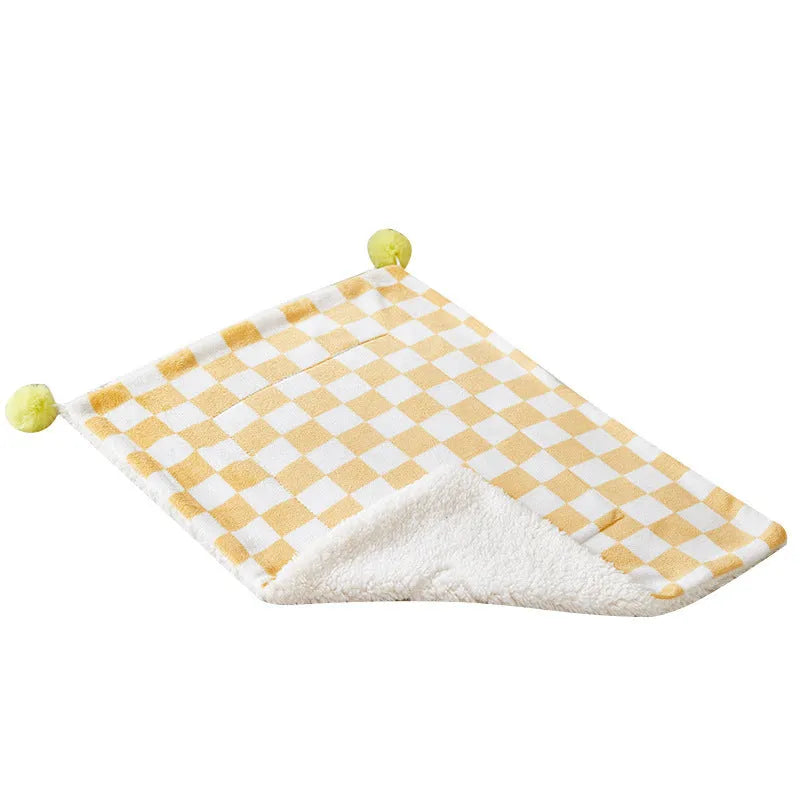 Plush pet blanket with plaid pattern and fur ball decoration on furniture with cat