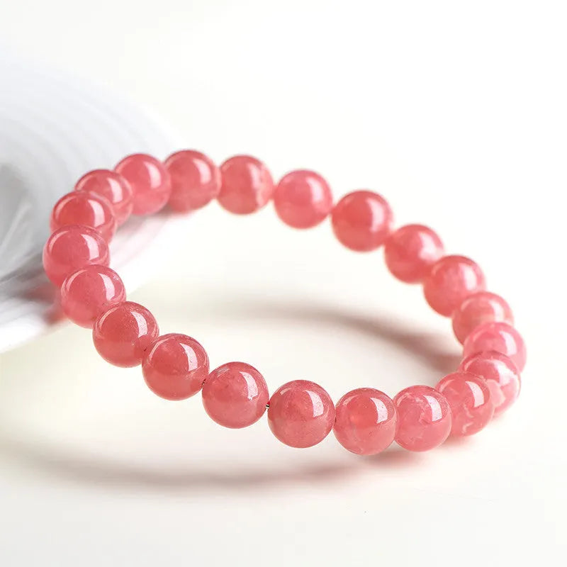 Women's geometric rhodochrosite crystal bracelet with a longevity lock charm on a wrist.