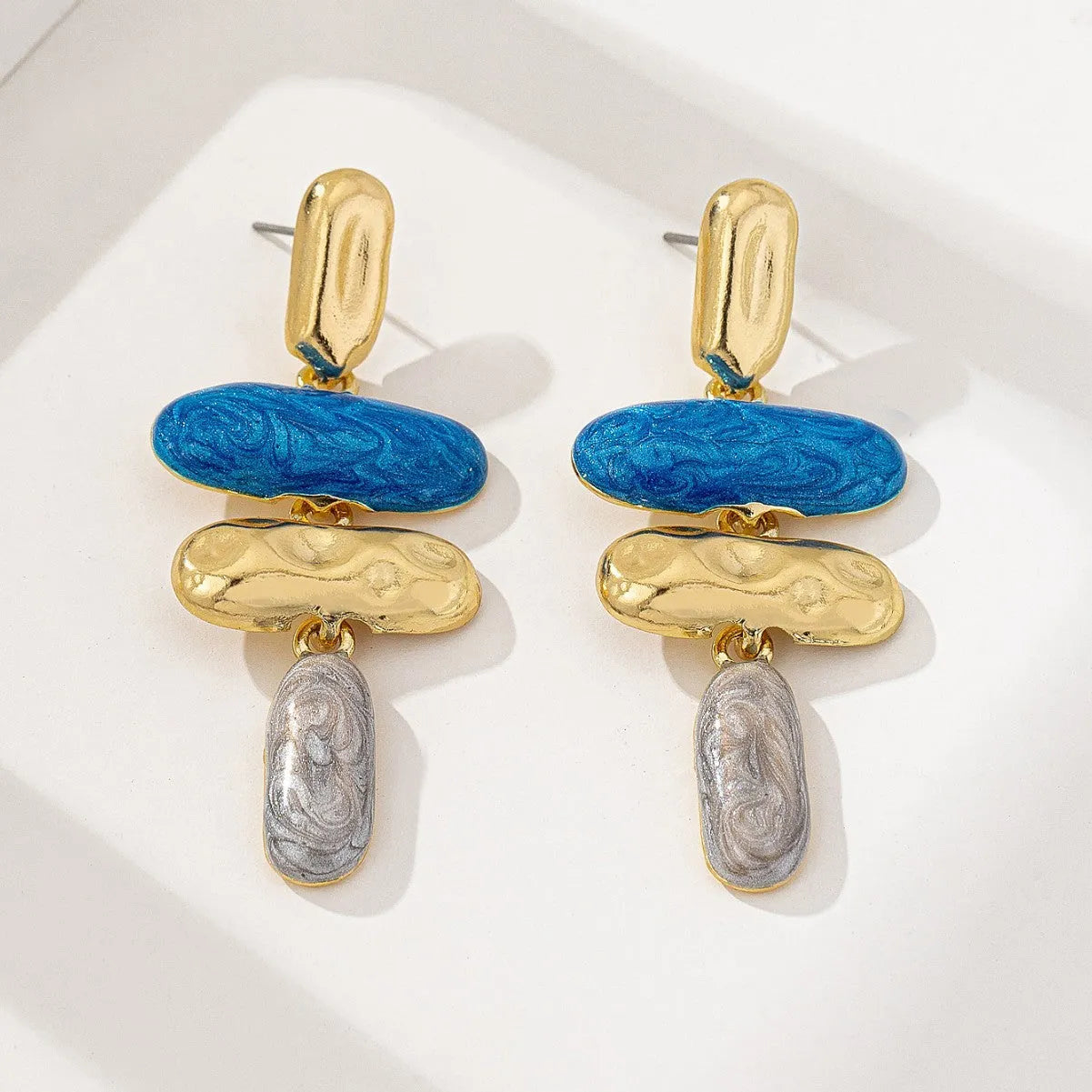 A pair of simple geometric stud earrings with a multicolour electroplated finish on a white background.