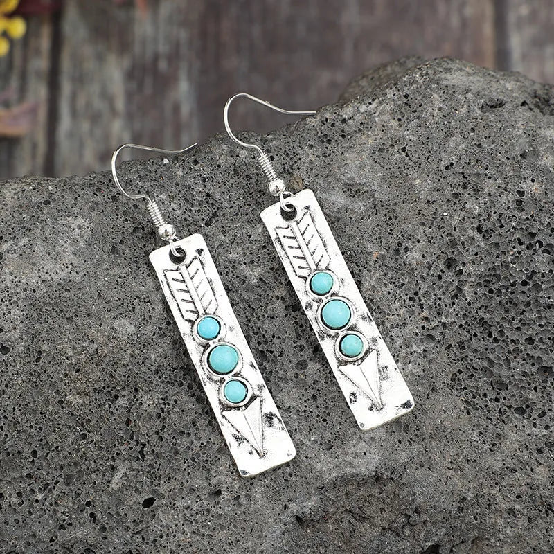 Geometric long silver earrings with blue turquoise inlay detail on a white background.