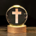 White crystal ball ornament on wood base with warm light and religious symbols