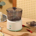 Mini electric food processor in light green with transparent cup and stainless steel blades on countertop.