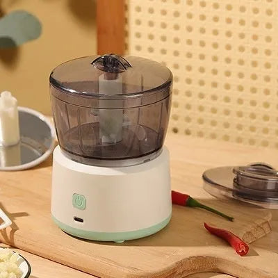 Mini electric food processor in light green with transparent cup and stainless steel blades on countertop.