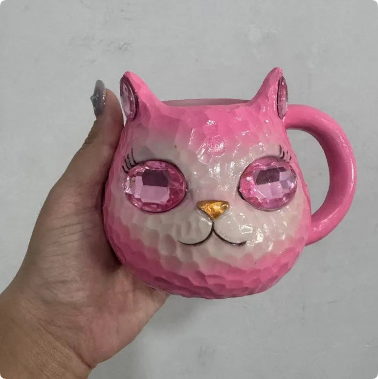 Colourful cat-shaped resin craft ornament in purple, green, blue, or pink on a desk.