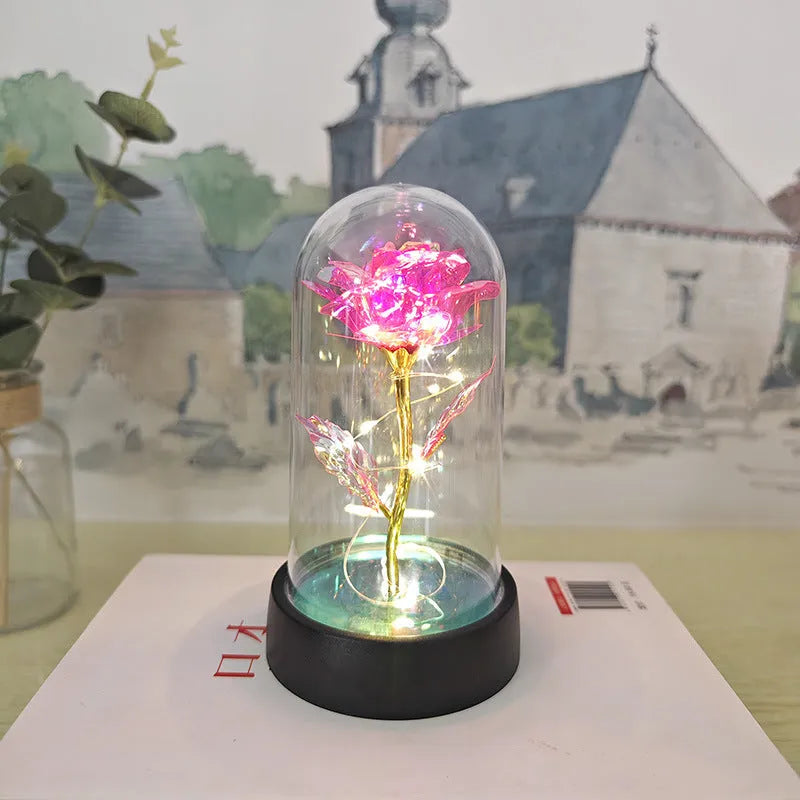 Small decorative table lamp with coloured LED lights illuminating plastic flowers under a glass dome.