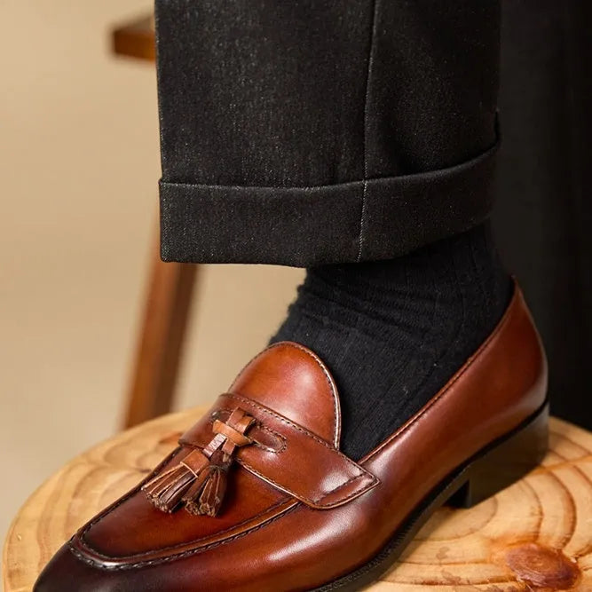 Men's black polished leather tassel loafers with a rubber sole on a white background.