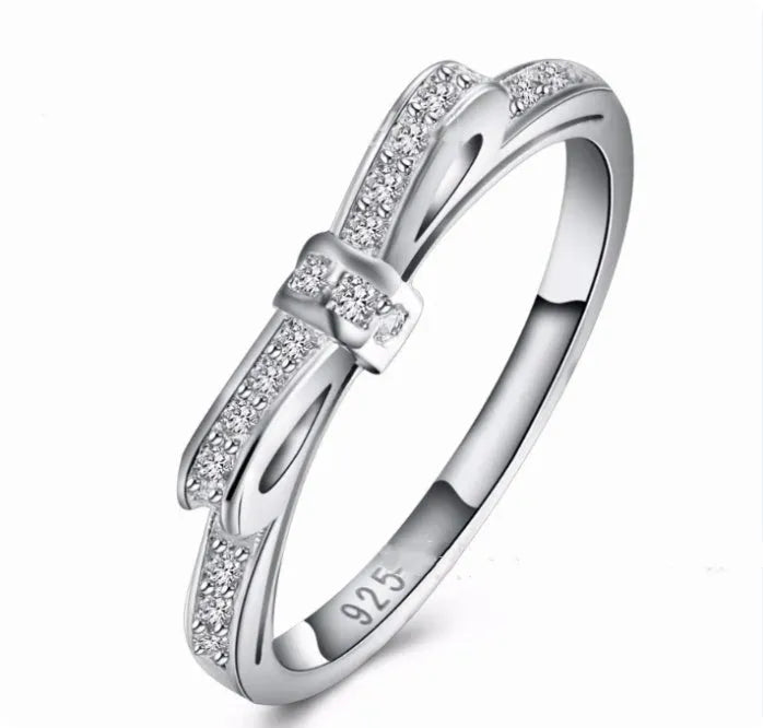 Silver coloured bow-shaped ring with zircon crystal details on a white background.