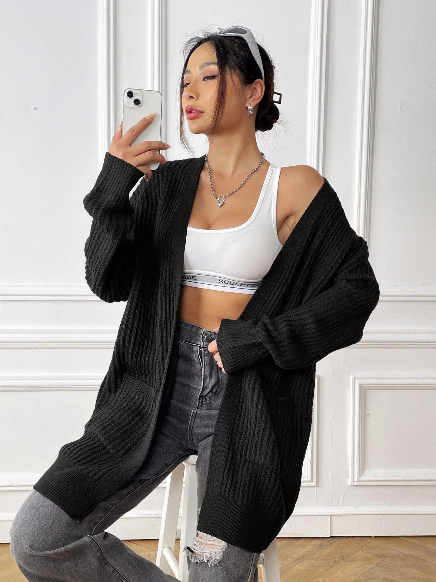 Women's dark green loose fit acrylic cardigan sweater with long sleeves on a hanger.