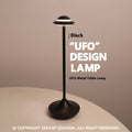 Creative metal UFO table lamp in black with touch dimming on a wooden desk.