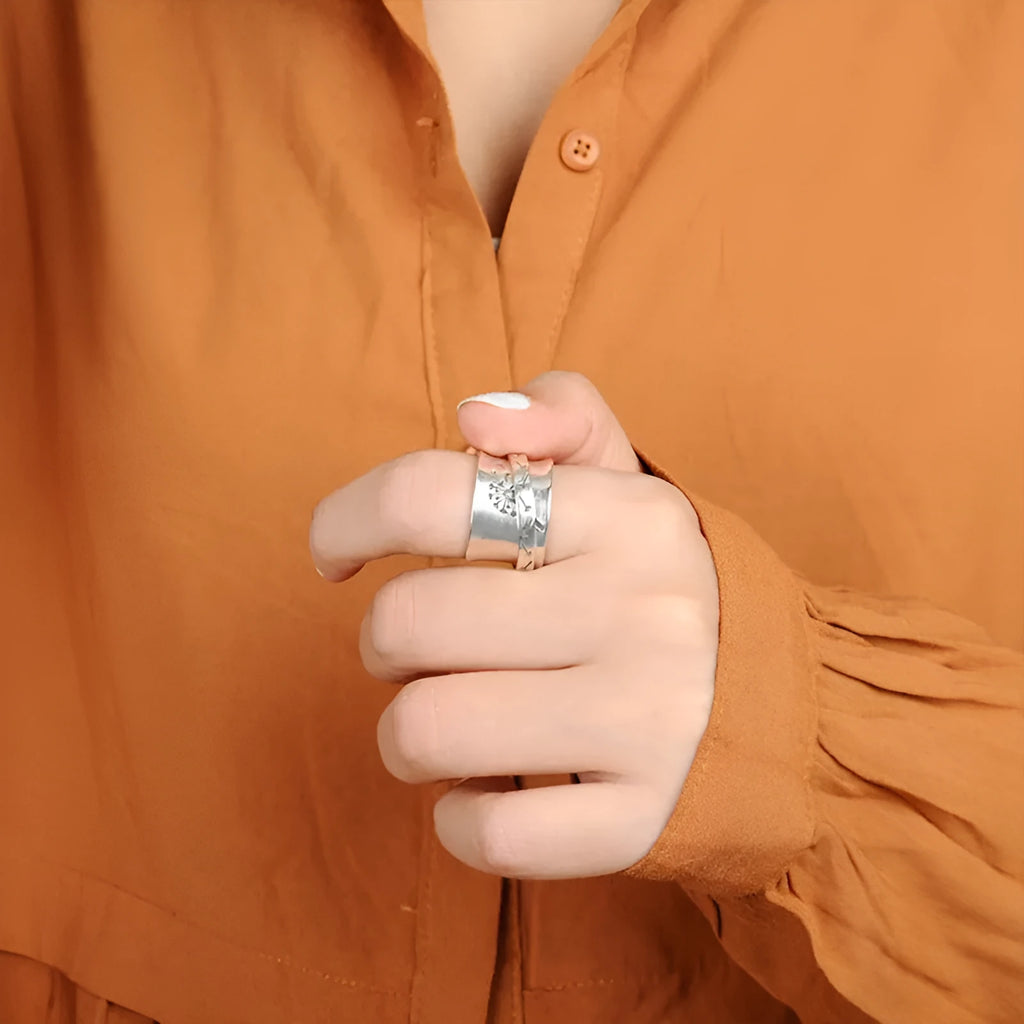 Silver coloured alloy flower ring with rotatable floral detail on a finger.