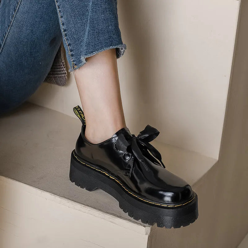 Women's black thick-soled lace-up shoes with ribbon and cross-strap design on a white background.
