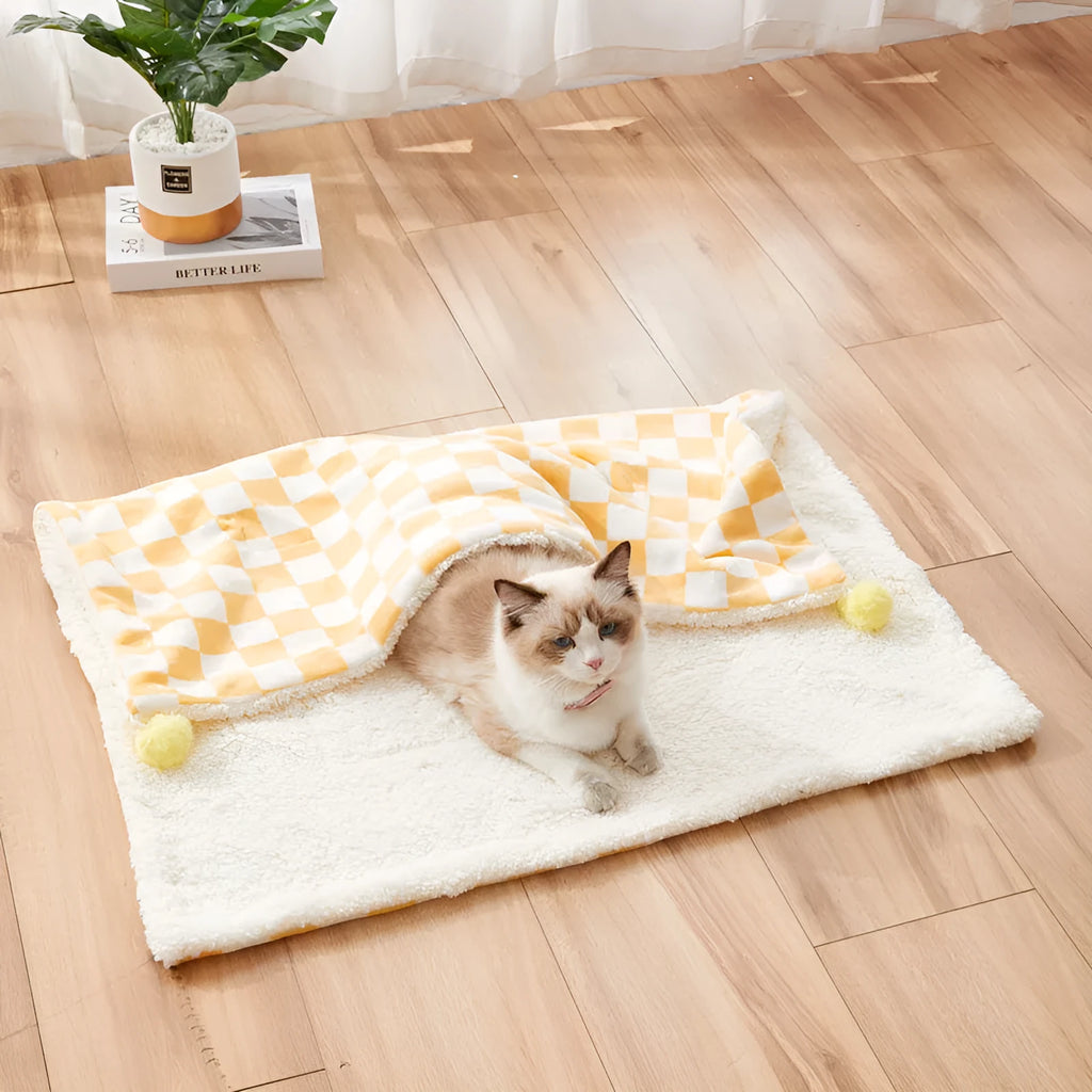 Plush pet blanket with plaid pattern and fur ball decoration on furniture with cat