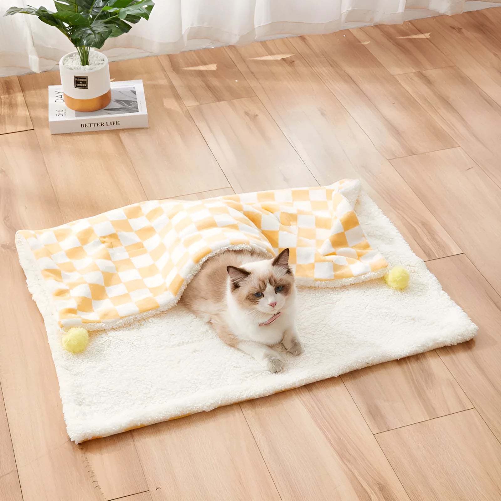 Plush pet blanket with plaid pattern and fur ball decoration on furniture with cat