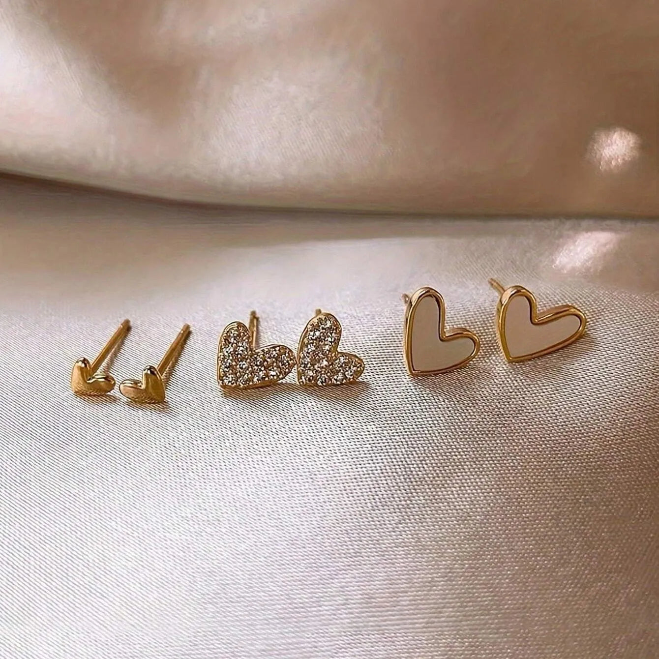 Three pairs of women's heart-shaped alloy earrings in gold, black, white, and pink colours