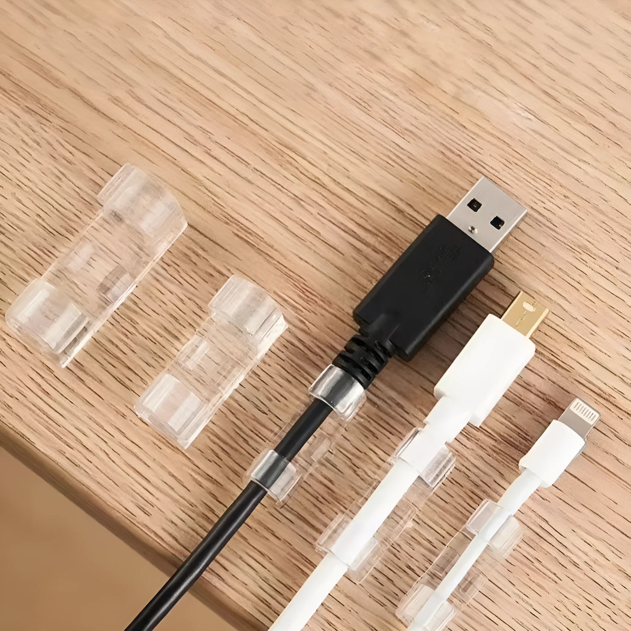 Transparent plastic self-adhesive cable clip holding a white wire against a wall.