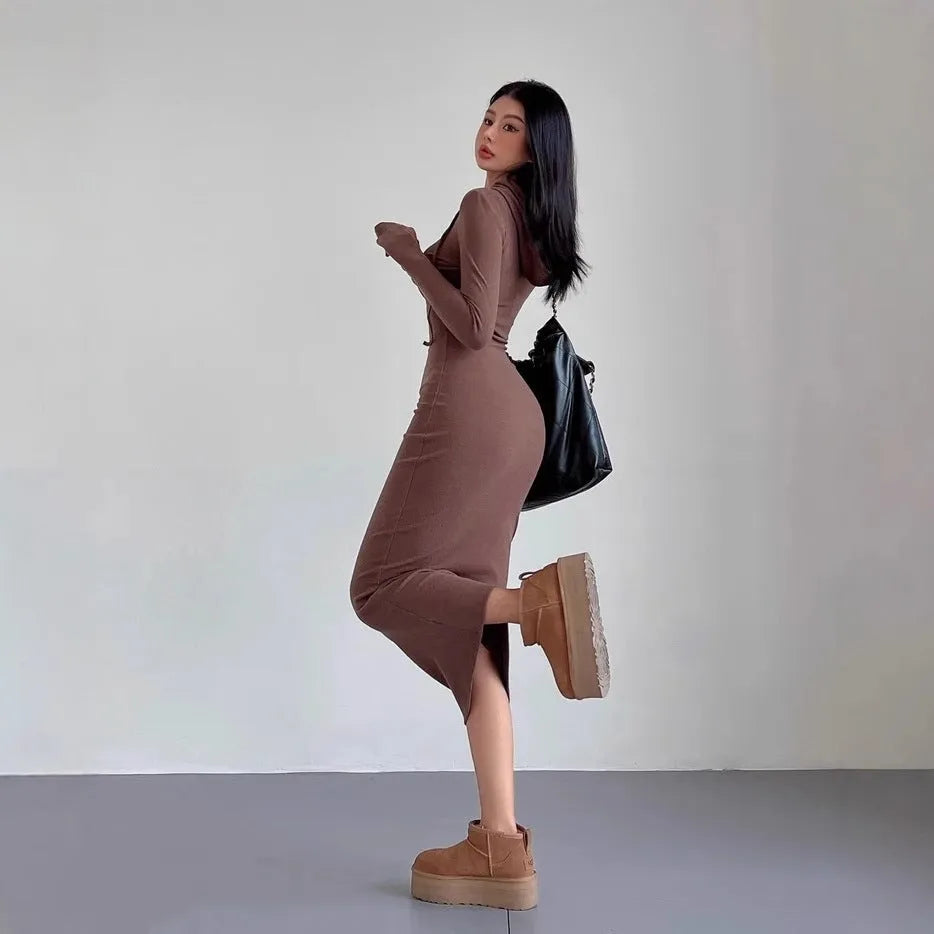 A woman wearing a light grey hooded sheath dress with long sleeves, showcasing the high waist and over-the-knee length.