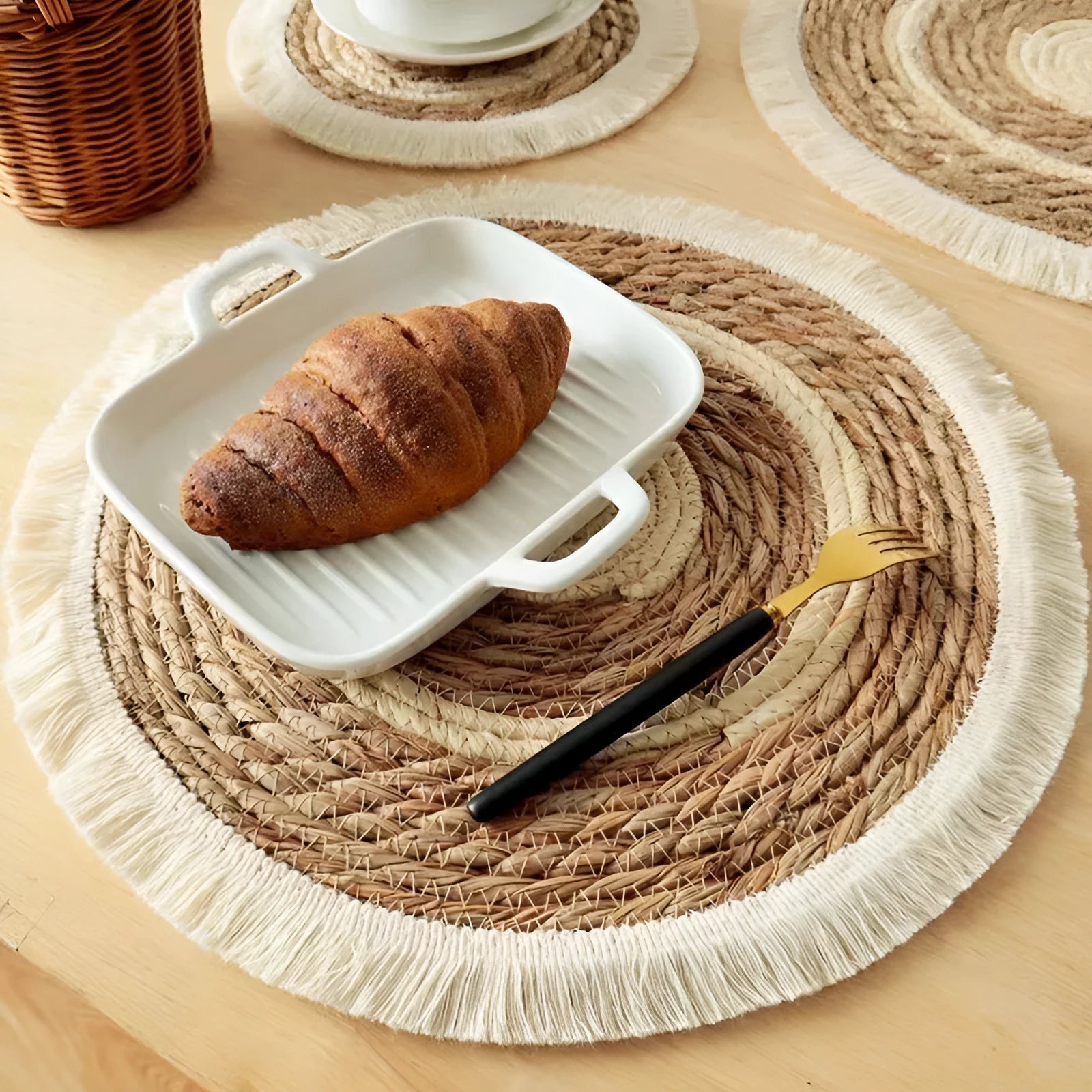 Round natural papyrus placemat with tassel trim on a wooden table.