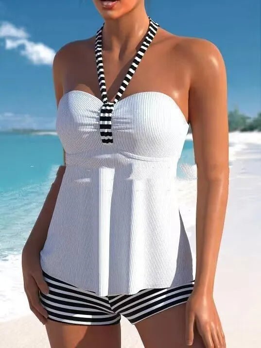 Woman modelling a black and white striped off-shoulder one-piece swimsuit on a beach.