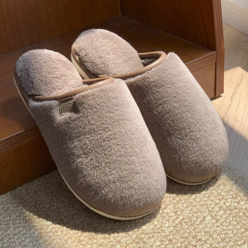 Pair of solid colour plush house slippers with PVC sole on a wooden floor.