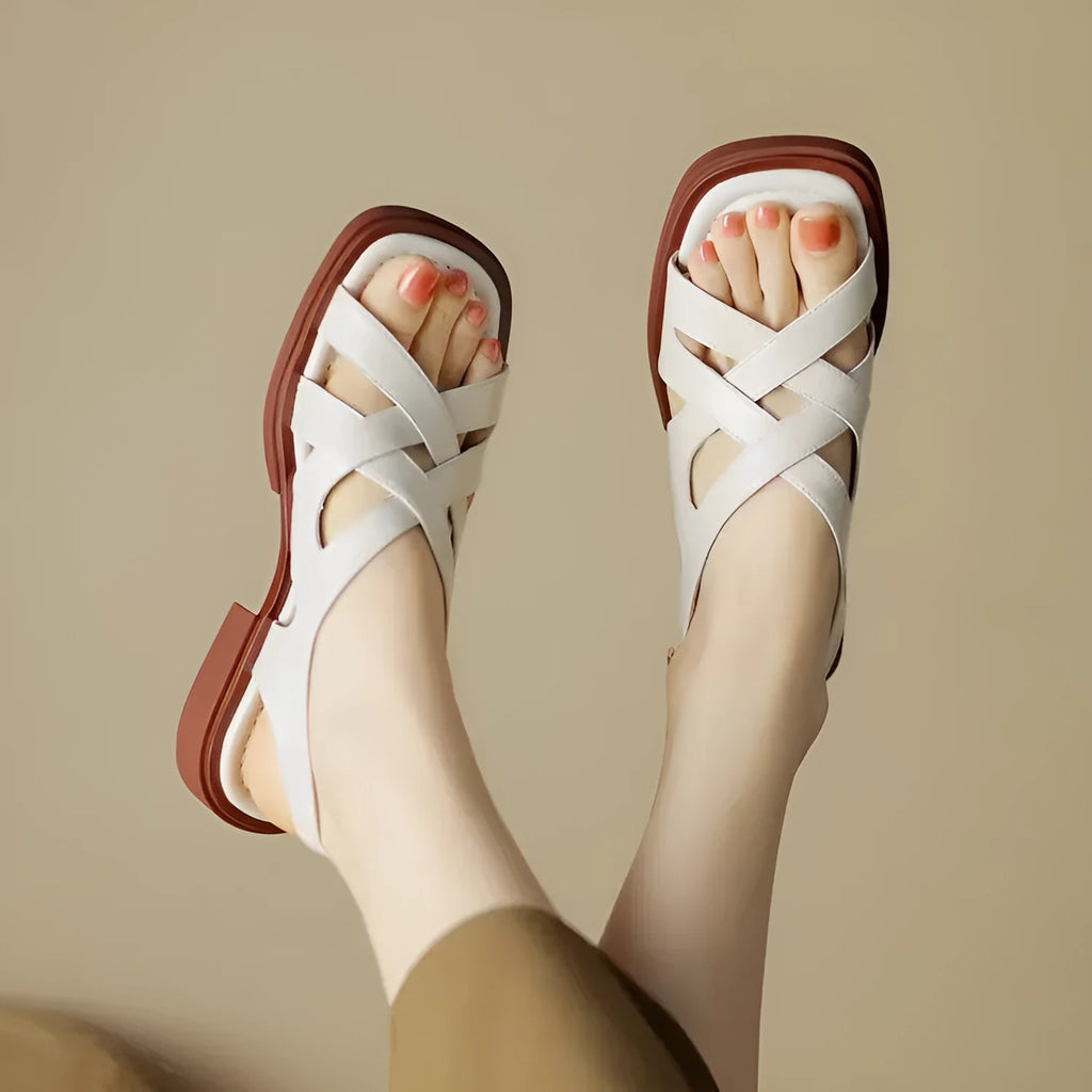 Glossy black patent leather women's sandals with a cross-band design, square toe, and low rubber sole.