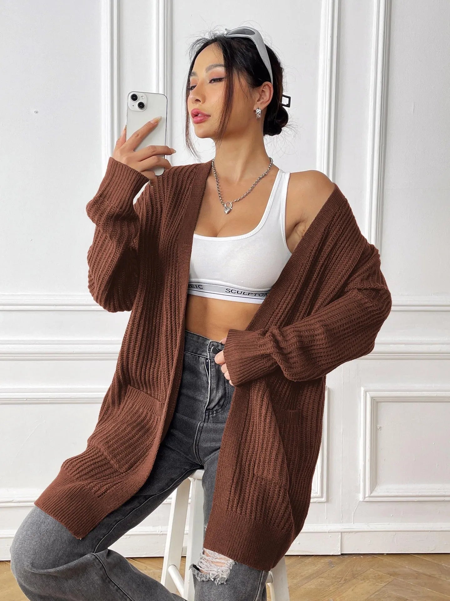 Women's dark green loose fit acrylic cardigan sweater with long sleeves on a hanger.