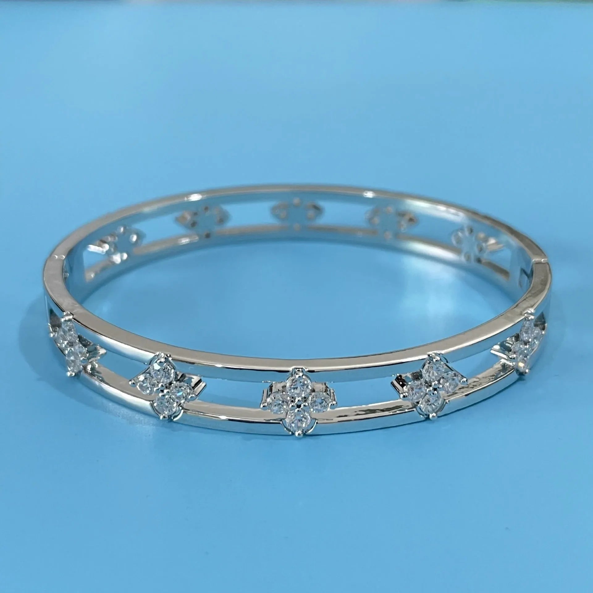 Gold and silver women's hollow bracelets with zircon stones and four-leaf clover charms on a white background.