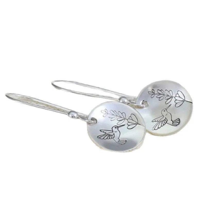 A pair of silver-coloured retro earrings with a glossy round shape featuring a detailed bird and leaf design.
