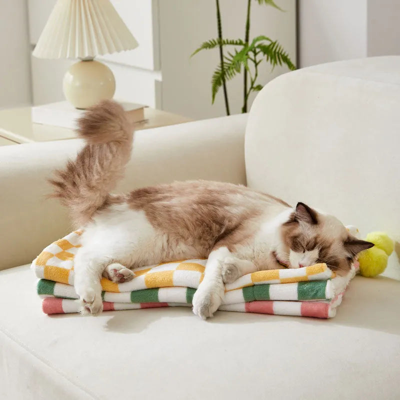 Plush pet blanket with plaid pattern and fur ball decoration on furniture with cat