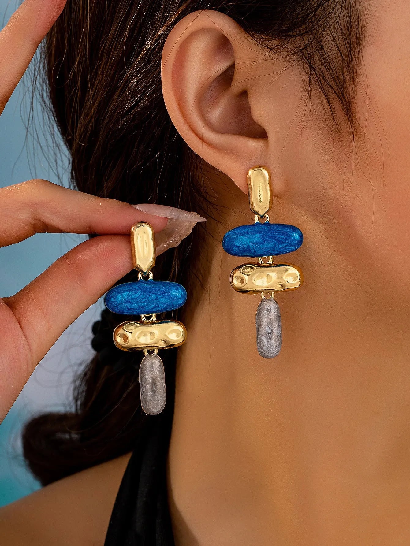 A pair of simple geometric stud earrings with a multicolour electroplated finish on a white background.