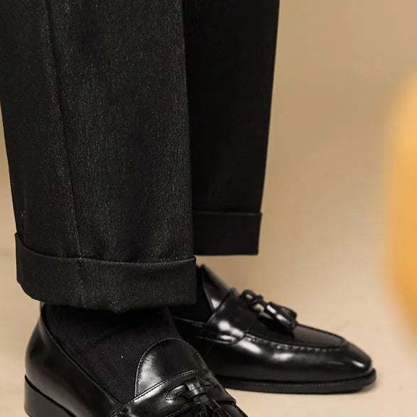 Men's black polished leather tassel loafers with a rubber sole on a white background.