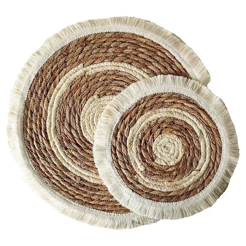 Round natural papyrus placemat with tassel trim on a wooden table.