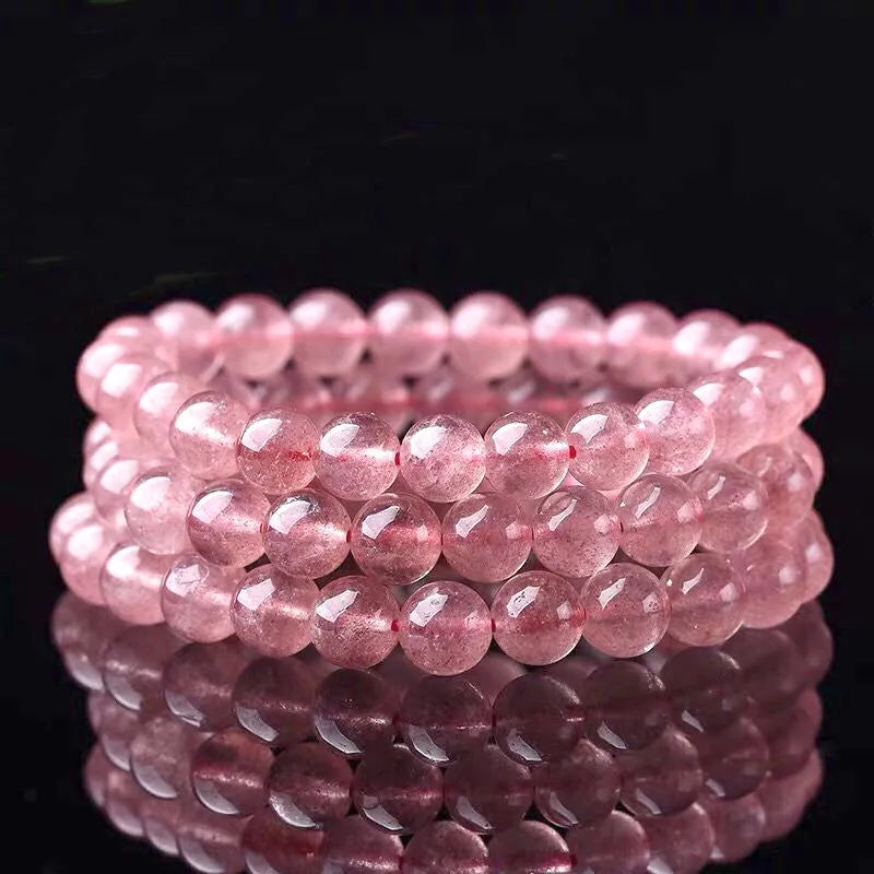 Women's strawberry quartz crystal bracelet with polished round beads on a white background.