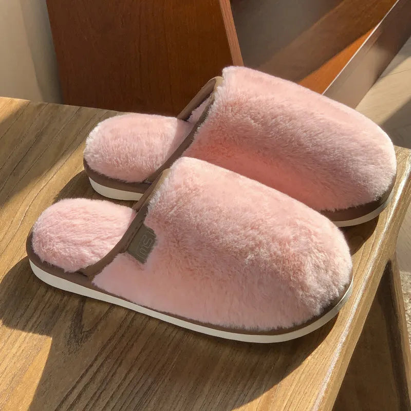 Pair of solid colour plush house slippers with PVC sole on a wooden floor.