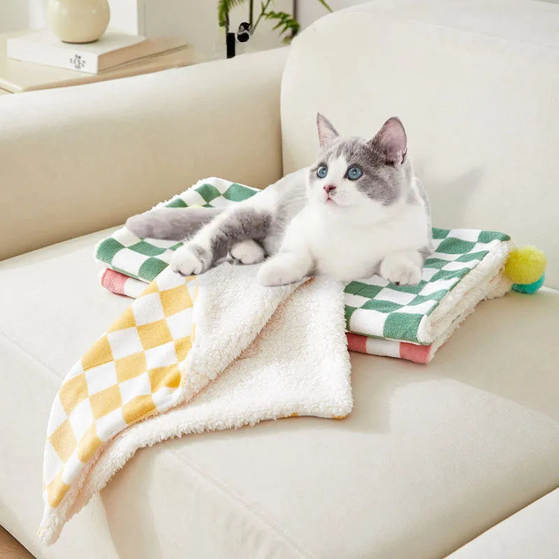 Plush pet blanket with plaid pattern and fur ball decoration on furniture with cat