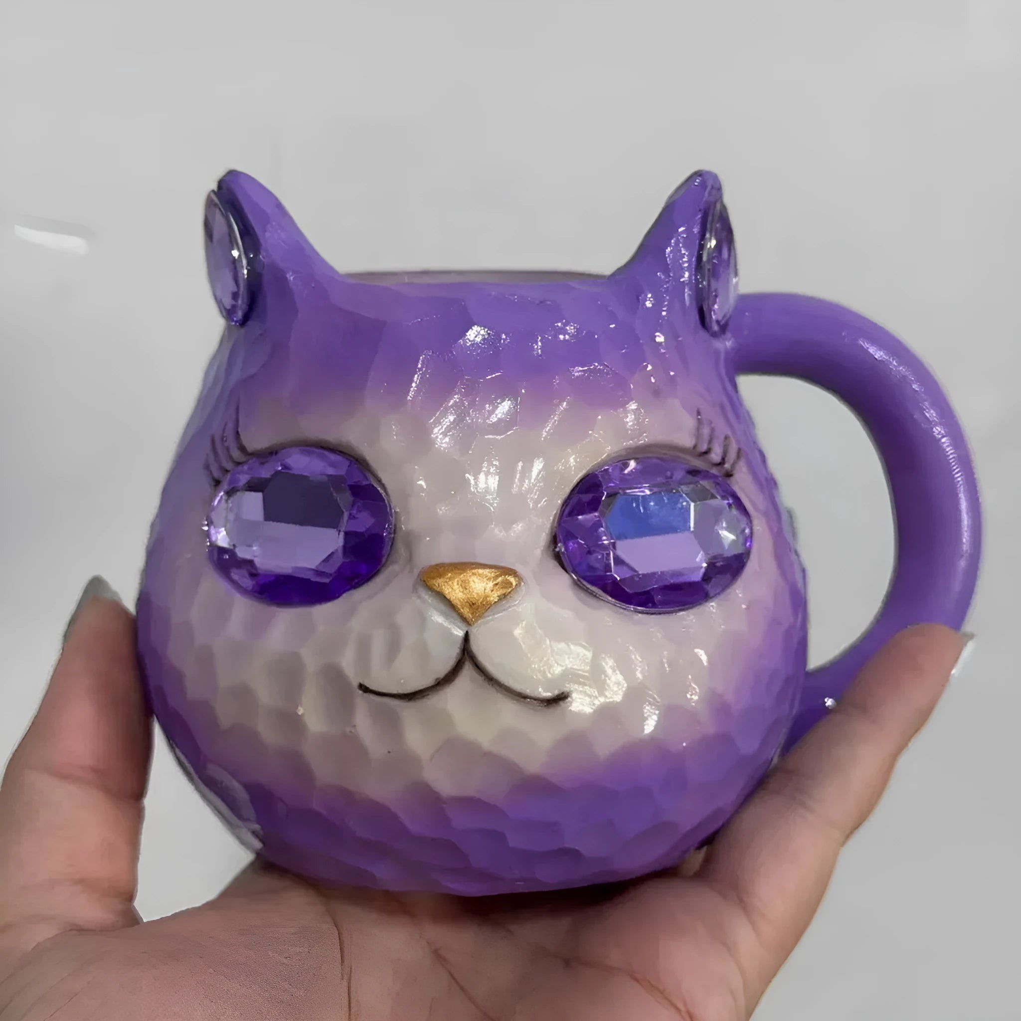 Colourful cat-shaped resin craft ornament in purple, green, blue, or pink on a desk.
