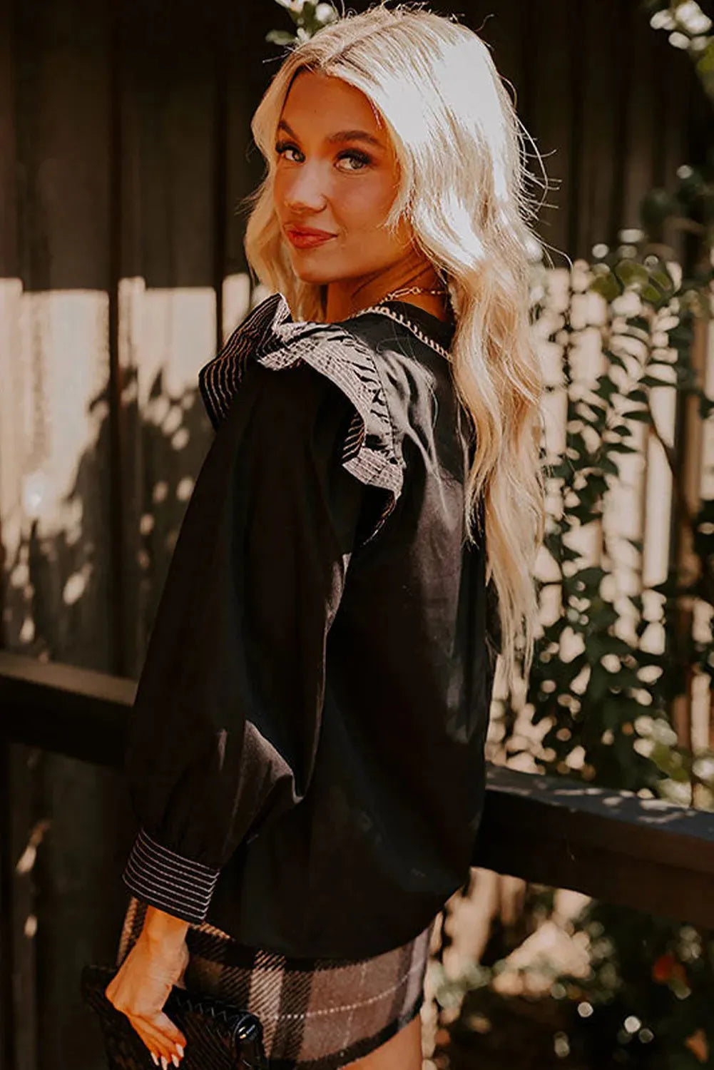 Black V-neck blouse with long ruffle sleeves and white contrast stitching.