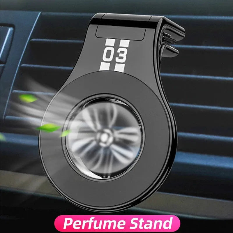 Black magnetic car phone holder clipped to a car air vent, showing adjustable paddle and fragrant slice.