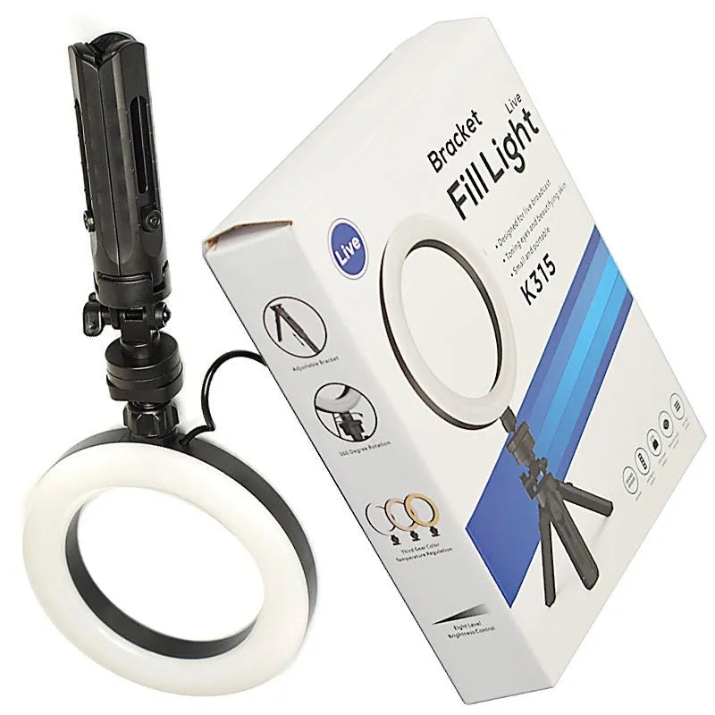 Black desktop tripod with adjustable fill light attached, holding a smartphone for streaming or video calls.