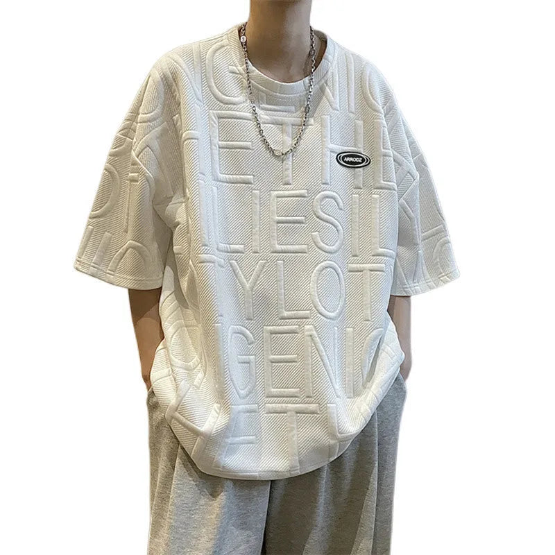 Man wearing a grey loose-fit T-shirt with a raised 3D retro letter print on the front.
