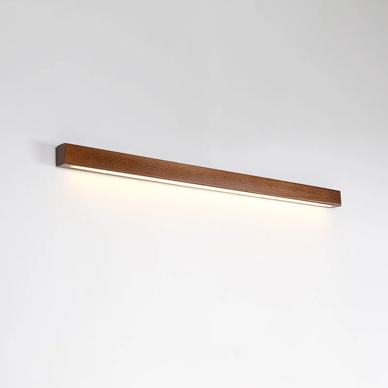 Walnut colour wood and acrylic wall lamp strip with LED lighting in a minimalist design on a wall.