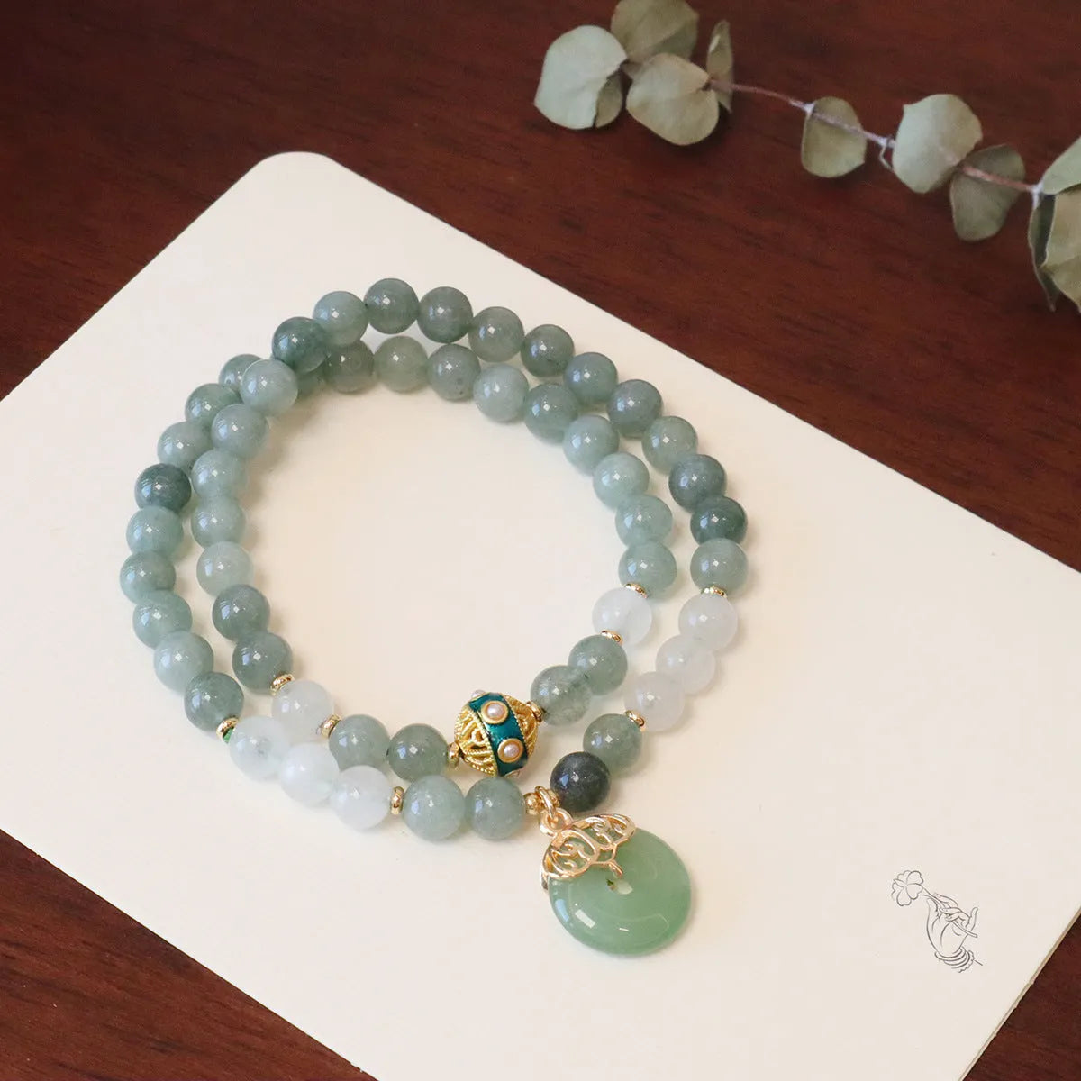 Close-up of a women's Myanmar jade bracelet with a geometric metal safety buckle pendant and lucky beads.