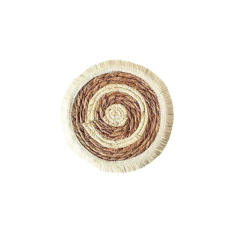 Round natural papyrus placemat with tassel trim on a wooden table.