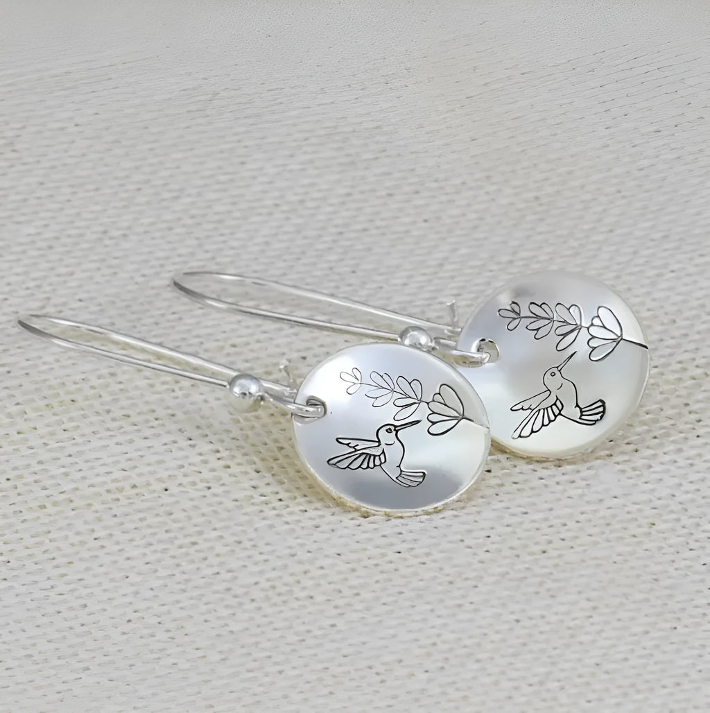 A pair of silver-coloured retro earrings with a glossy round shape featuring a detailed bird and leaf design.