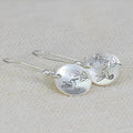 A pair of silver-coloured retro earrings with a glossy round shape featuring a detailed bird and leaf design.