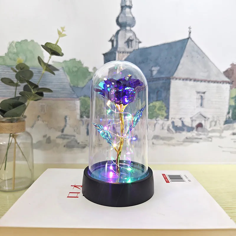 Small decorative table lamp with coloured LED lights illuminating plastic flowers under a glass dome.
