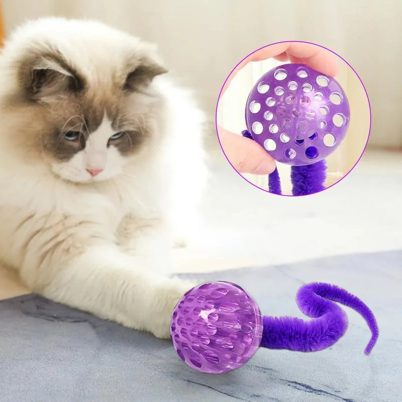 Green TPR bouncy ball with pink plush worm tail cat toy on floor