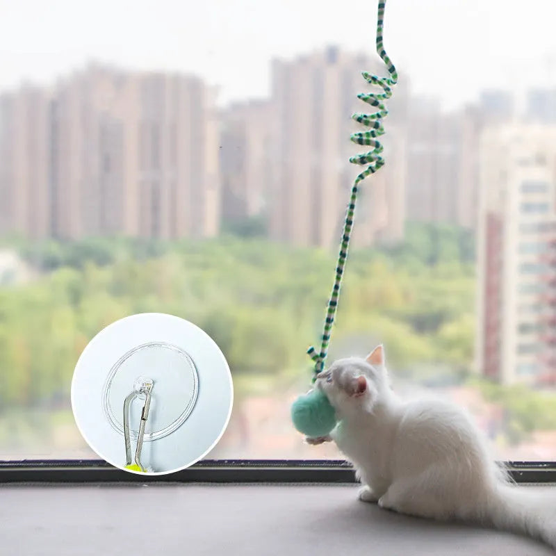 Hanging cat toy with bell stick and red inflatable ball attached to a glass door by a suction cup.