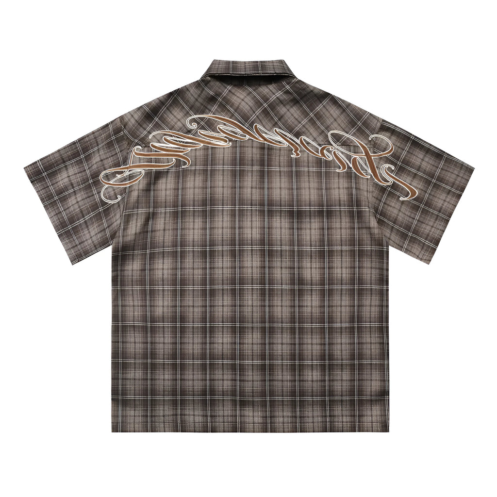 Man wearing a black and brown plaid short sleeve shirt with embroidered letter on lapel