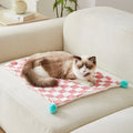 Plush pet blanket with plaid pattern and fur ball decoration on furniture with cat